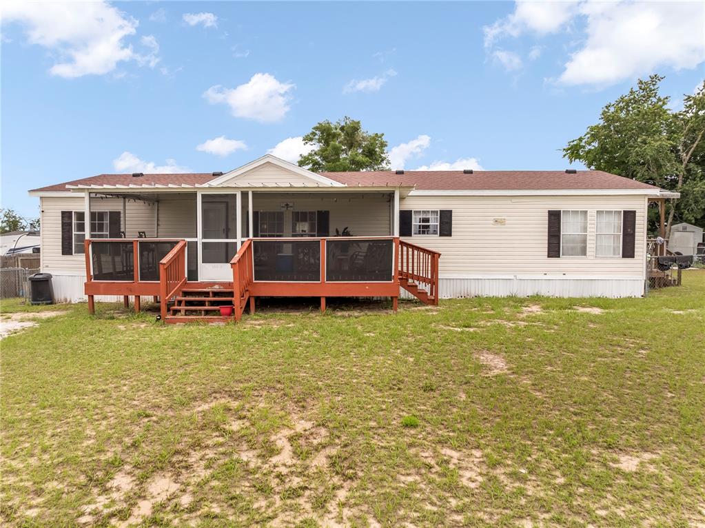 A single-story manufactured home features a large wooden deck with a screened-in porch area — 14205 SE 60TH AVENUE, SUMMERFIELD, FL