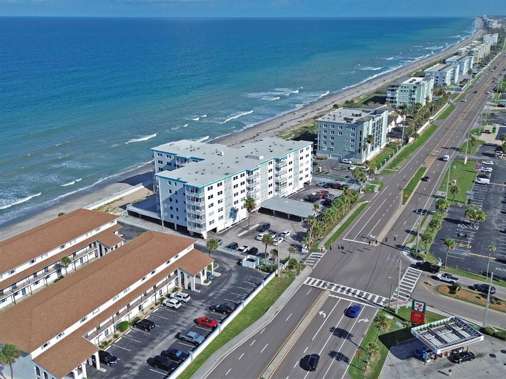 An aerial view shows a multi-story beachfront condominium complex with a parking lot and road — 205 HIGHWAY A1A #501 UNIT 501, SATELLITE BEACH, FL