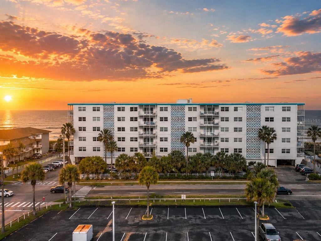 An exterior view of a multi-story apartment building at sunset with palm trees and parking — 205 HIGHWAY A1A #501 UNIT 501, SATELLITE BEACH, FL