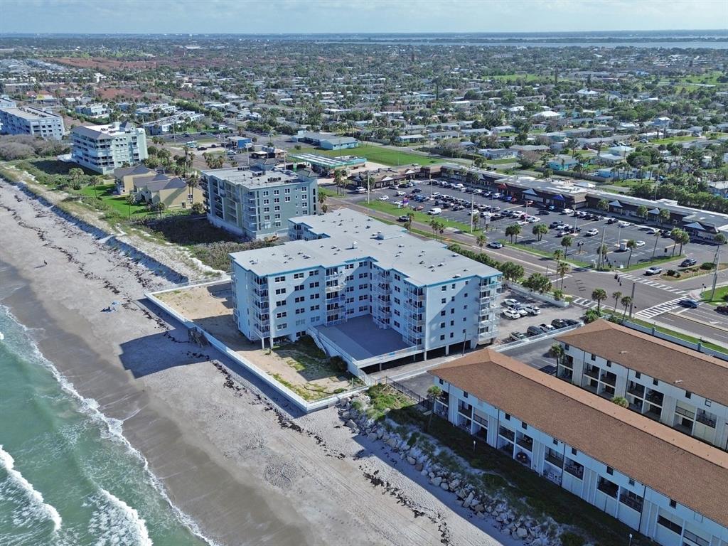 An aerial view shows a multi-story beachfront condominium building situated next to a parking lot — 205 HIGHWAY A1A #501 UNIT 501, SATELLITE BEACH, FL