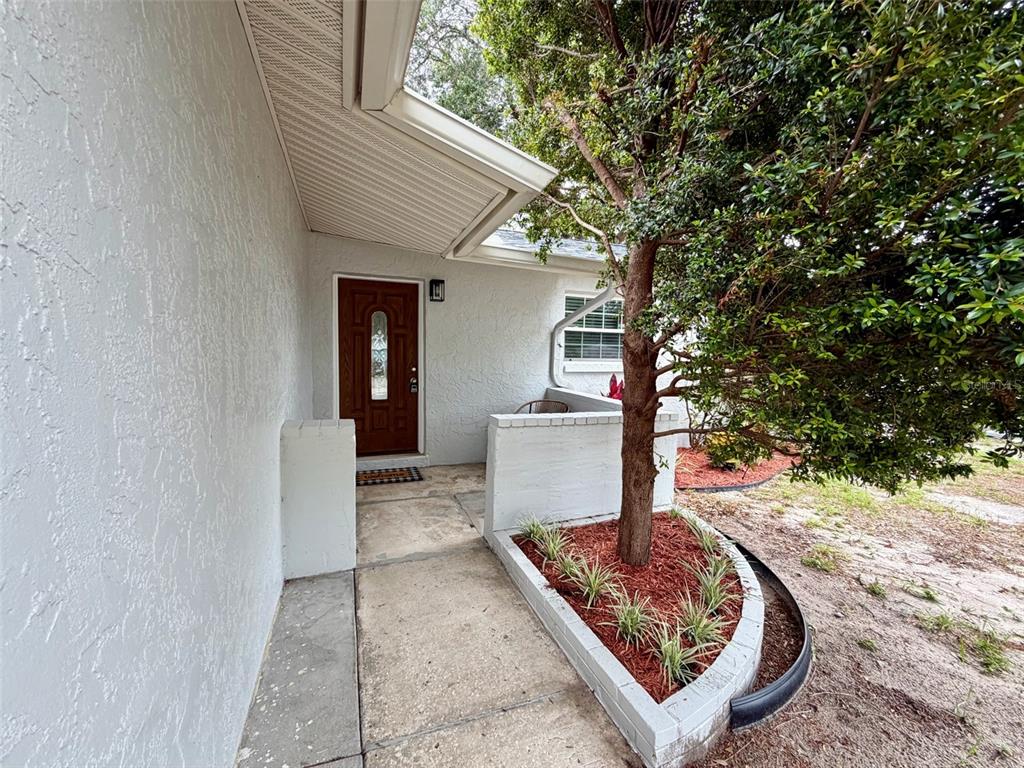 A white stucco house exterior features a brown front door and a curved brick planter — 6945 ORKNEY AVENUE N, ST PETERSBURG, FL