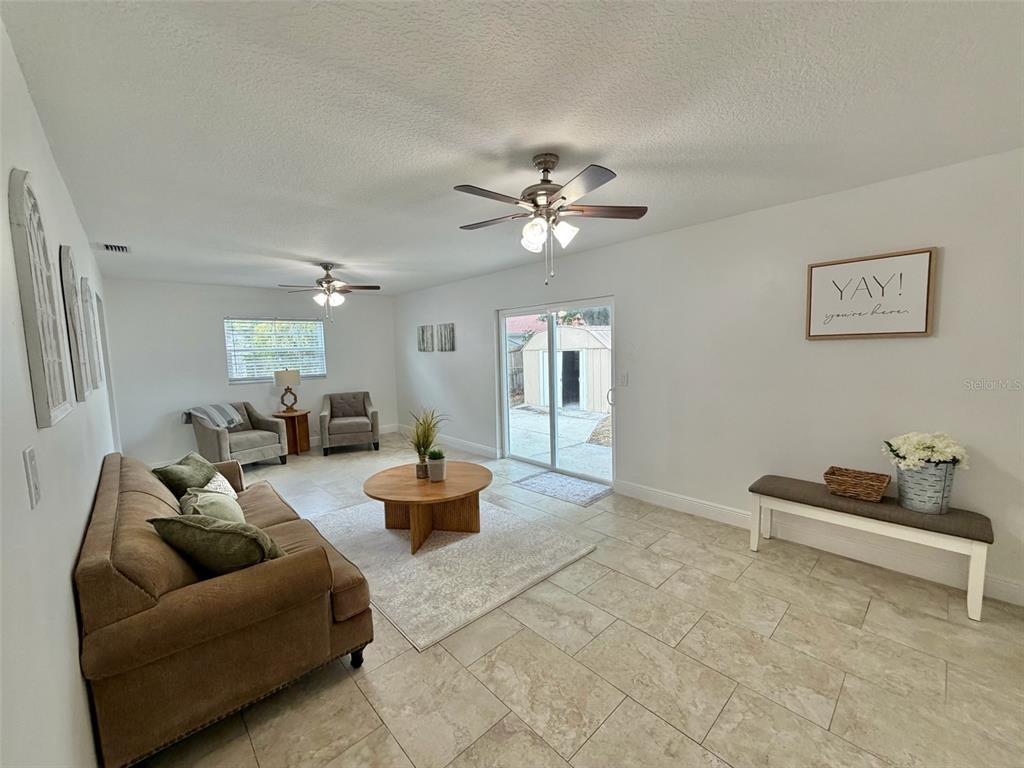A living room features tile flooring, two ceiling fans, a brown sofa, and sliding glass doors — 6945 ORKNEY AVENUE N, ST PETERSBURG, FL