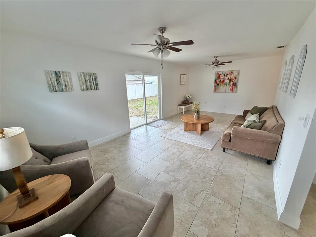 A living room with tile flooring, two ceiling fans, a sofa, chairs, and sliding doors — 6945 ORKNEY AVENUE N, ST PETERSBURG, FL