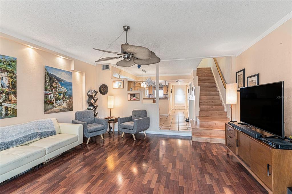 A living room features wood flooring, a ceiling fan, two gray chairs, and a staircase — 12465 2ND STREET E UNIT 105B, TREASURE ISLAND, FL