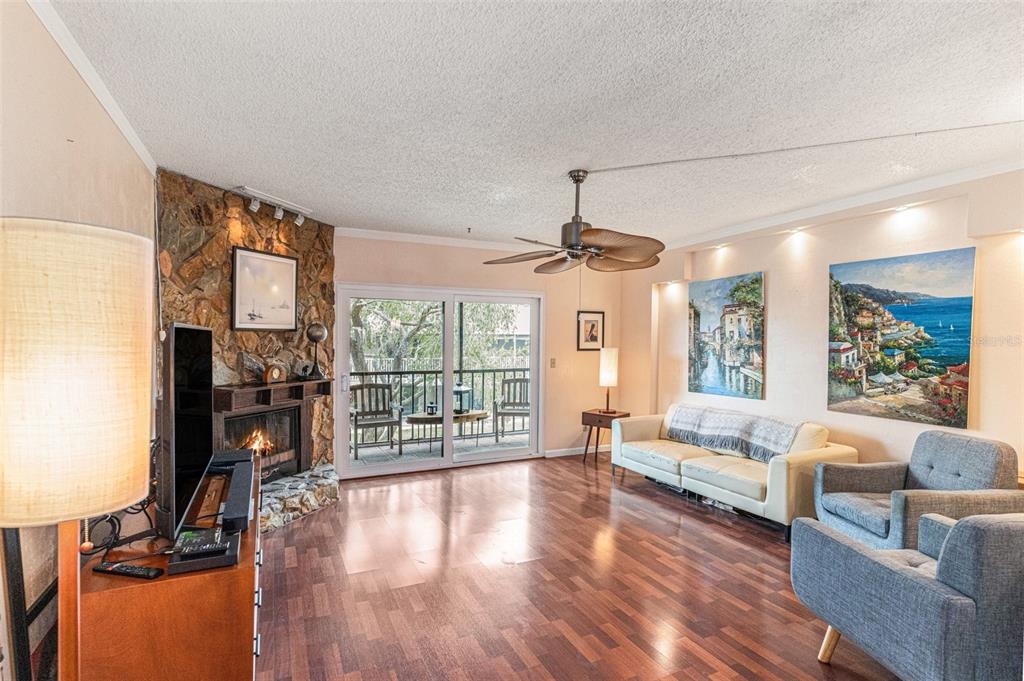 A living room features a stone fireplace, wood flooring, a ceiling fan, and a balcony — 12465 2ND STREET E UNIT 105B, TREASURE ISLAND, FL
