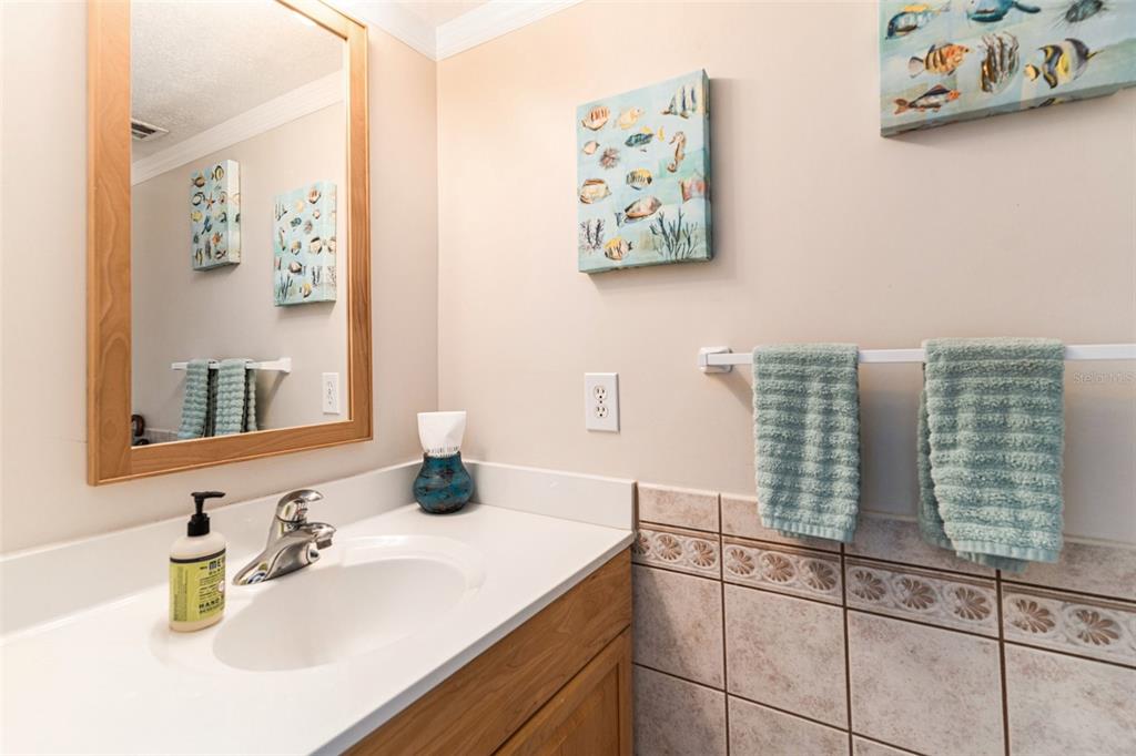 A bathroom vanity features a white countertop, wooden cabinet, mirror, and coastal-themed wall art — 12465 2ND STREET E UNIT 105B, TREASURE ISLAND, FL