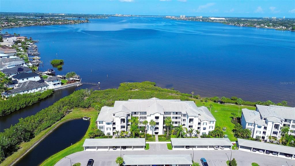 An aerial view shows a multi-story apartment complex with covered parking near a large bay — 850 TIDEWATER SHORES LOOP UNIT 402, BRADENTON, FL
