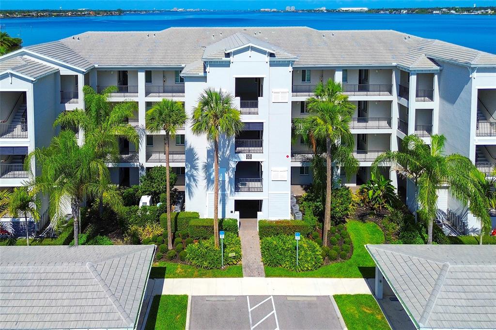 An aerial view of a multi-story apartment building with palm trees and a waterfront background — 850 TIDEWATER SHORES LOOP UNIT 402, BRADENTON, FL