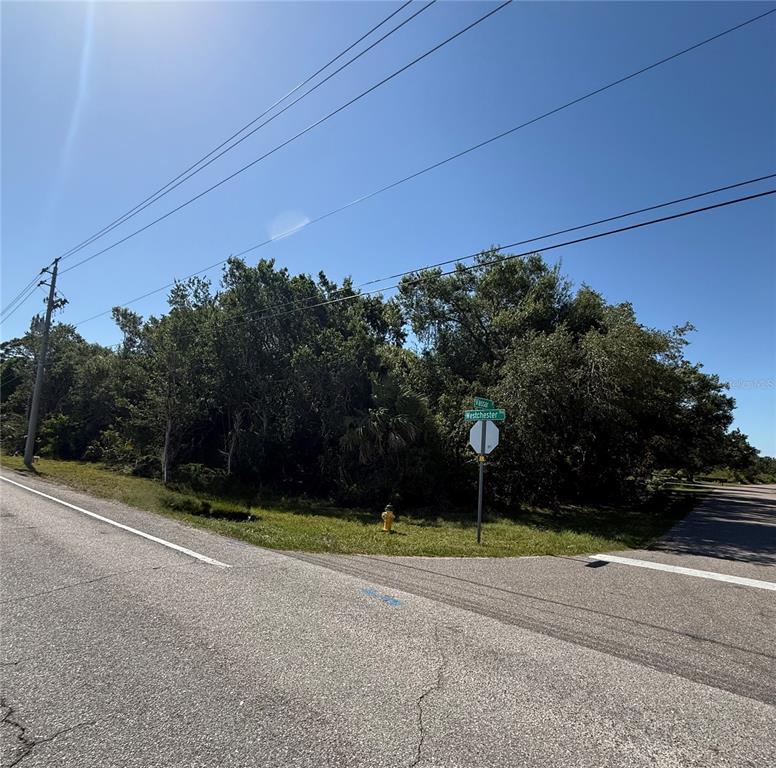 A vacant, tree-covered corner lot features a street sign and a fire hydrant — 23124 WESTCHESTER BOULEVARD, PUNTA GORDA, FL