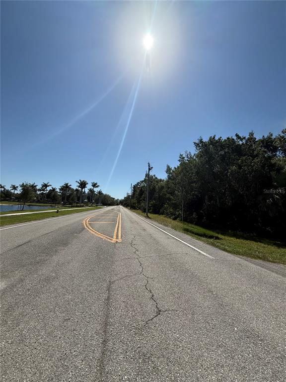 A paved road stretches toward the horizon under a bright sun with trees and water — 23124 WESTCHESTER BOULEVARD, PUNTA GORDA, FL