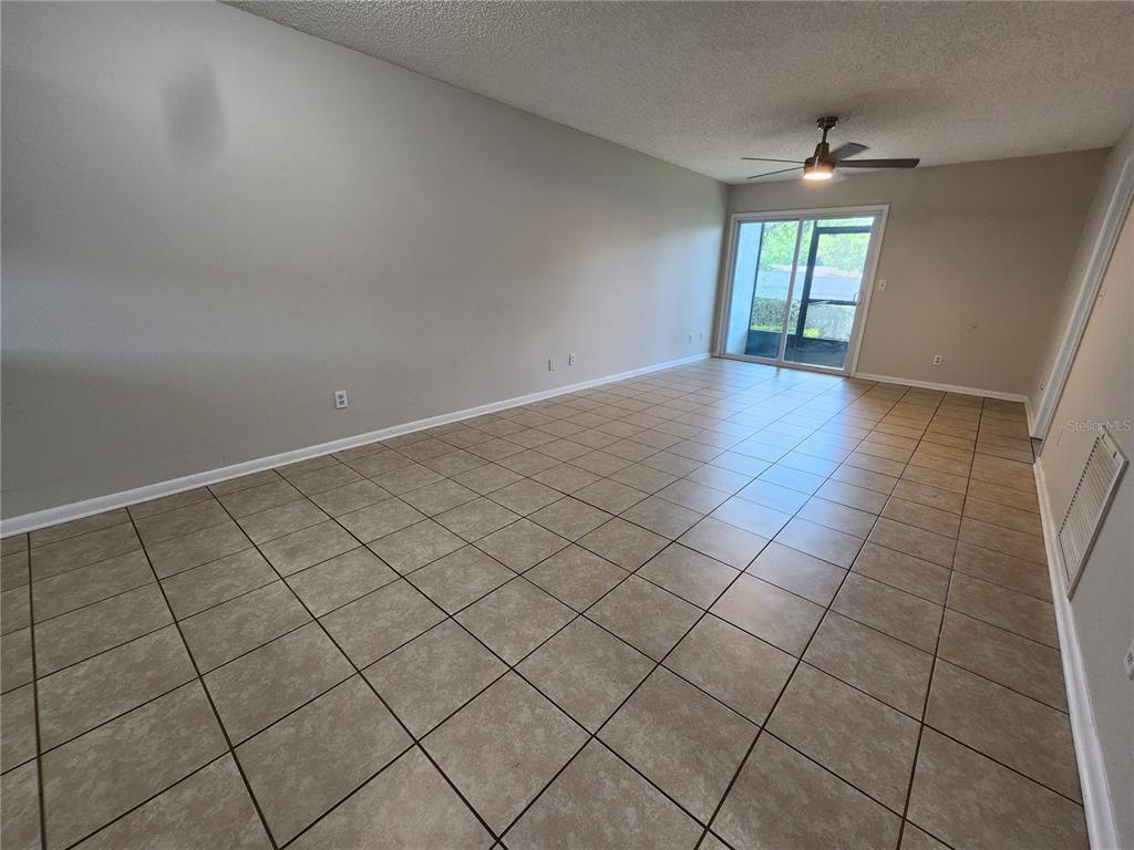 An empty living room features beige tile flooring, light gray walls, and a ceiling fan — 39132 COUNTY ROAD 54 UNIT 2152, ZEPHYRHILLS, FL