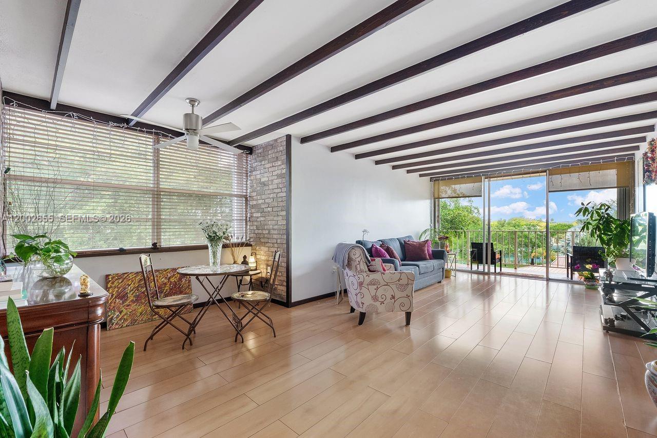 A living room features light wood flooring, exposed ceiling beams, and a brick accent wall — 13100 SW 92nd Ave, Miami FL 33176, MIAMI, FL
