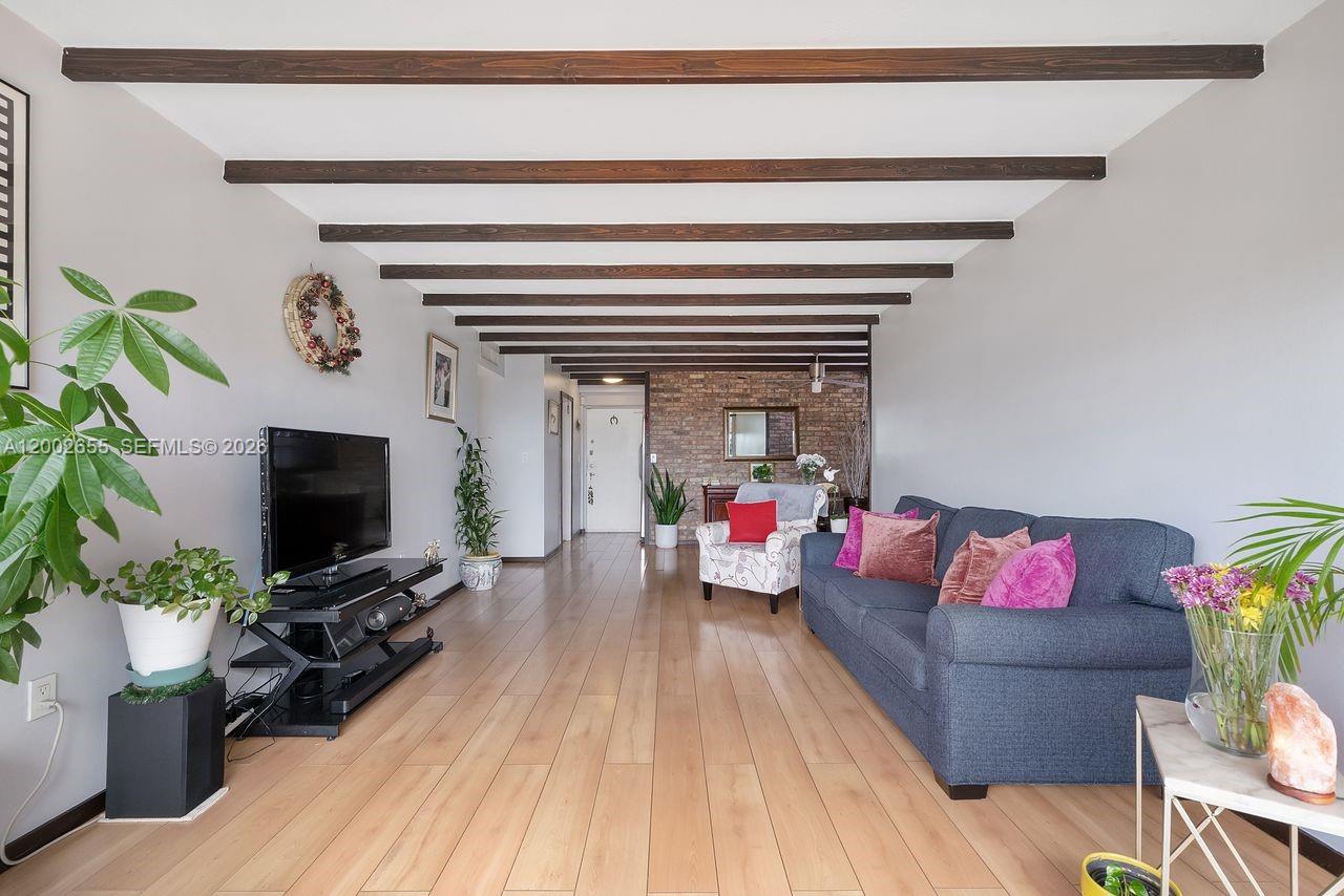 A living room features wood-look flooring, exposed ceiling beams, and a brick accent wall — 13100 SW 92nd Ave, Miami FL 33176, MIAMI, FL