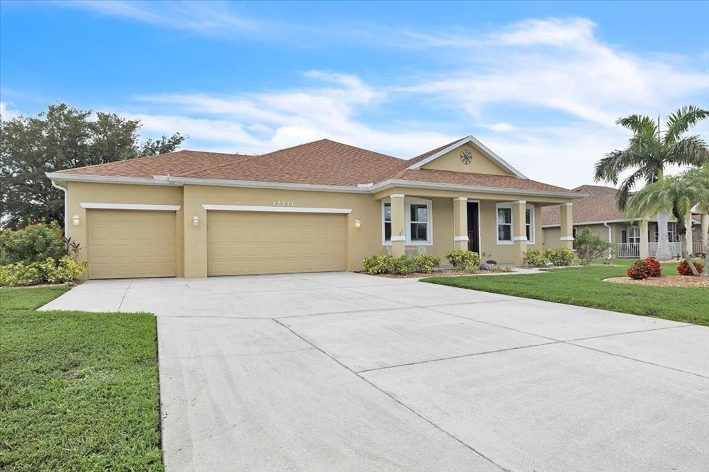 A tan single-story house with a three-car garage and a concrete driveway — 12933 SW PEMBROKE CIRCLE S, LAKE SUZY, FL
