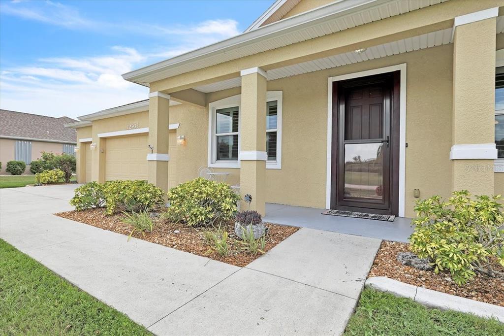 The exterior of a tan house features a covered porch, a dark front door, and landscaping — 12933 SW PEMBROKE CIRCLE S, LAKE SUZY, FL