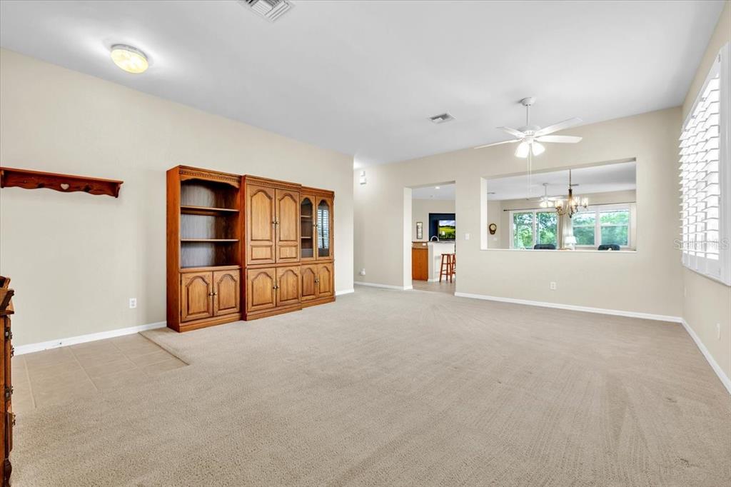 A carpeted living room features a large wooden wall unit and a view into the kitchen — 12933 SW PEMBROKE CIRCLE S, LAKE SUZY, FL