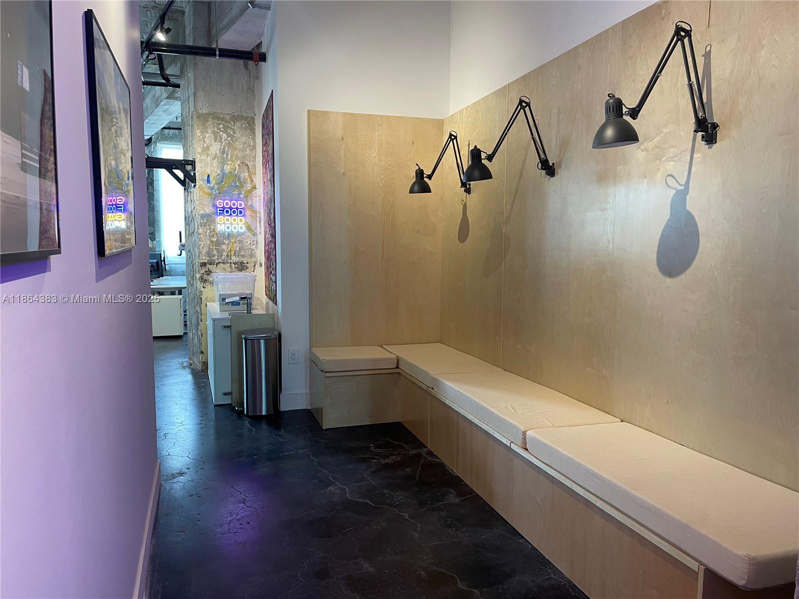 A waiting area features a built-in wooden bench, wall-mounted lamps, and a concrete floor — 1900 NE Miami Ct, Miami FL 33132, MIAMI, FL
