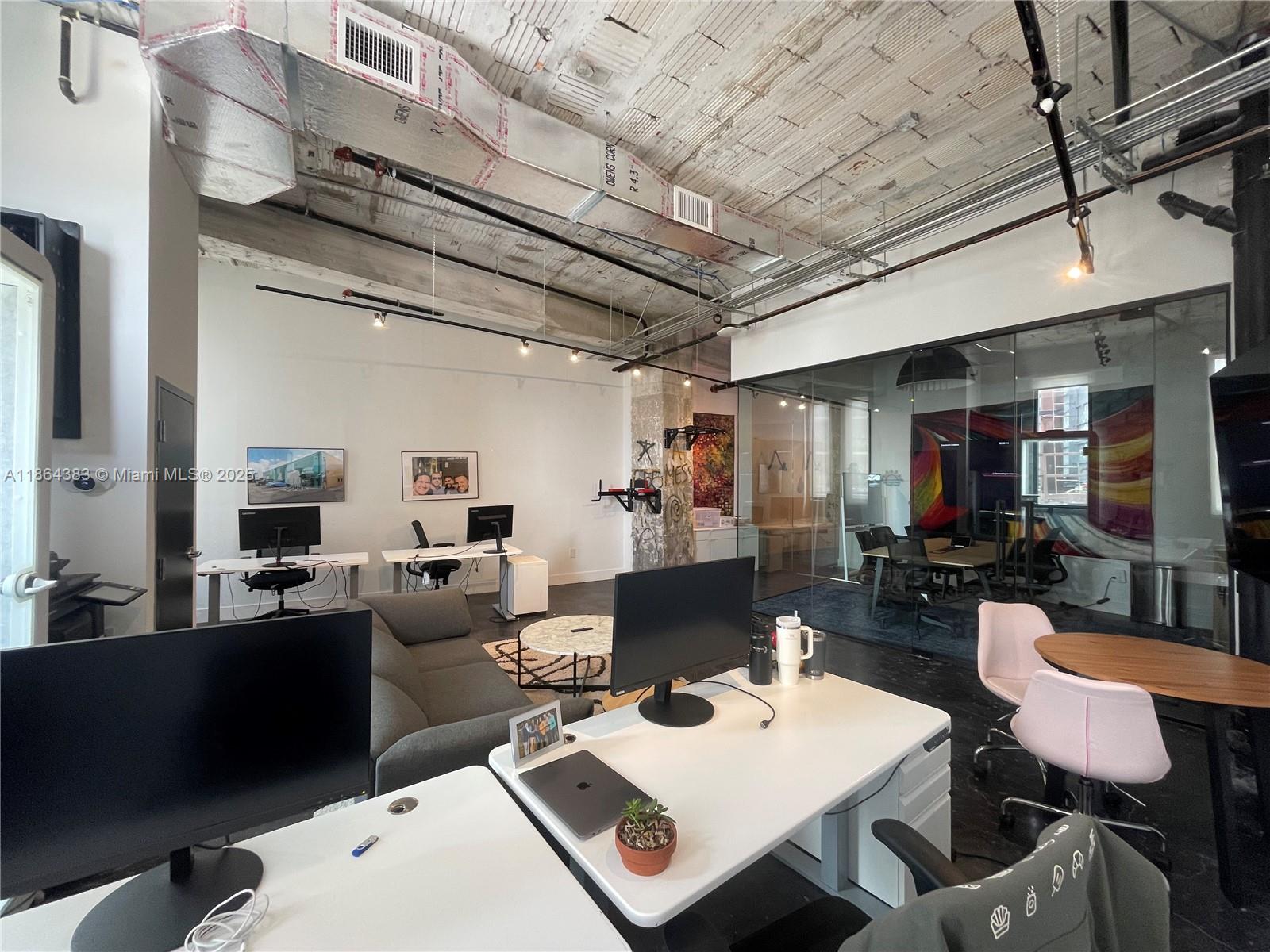 An open-plan office features exposed concrete ceilings, industrial ductwork, glass-walled conference rooms, and modern desks — 1900 NE Miami Ct, Miami FL 33132, MIAMI, FL