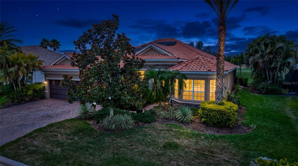 A single-story house with a tiled roof and brick driveway is shown at twilight — 7511 HERITAGE GRAND PLACE, BRADENTON, FL