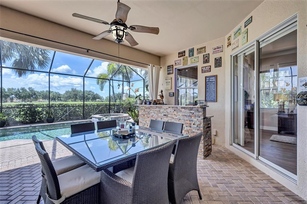 A covered patio features a dining set, a stone bar, and a view of a pool — 7511 HERITAGE GRAND PLACE, BRADENTON, FL