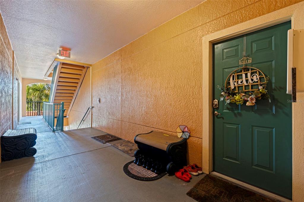 An outdoor apartment walkway features a green door with a hello wreath and stairs — 2773 VIA CIPRIANI UNIT 1321B, CLEARWATER, FL