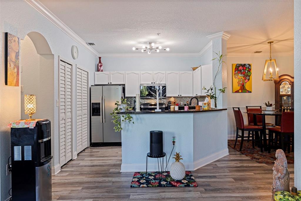 A kitchen with white cabinets, stainless steel appliances, and a breakfast bar opens to a dining area — 2773 VIA CIPRIANI UNIT 1321B, CLEARWATER, FL