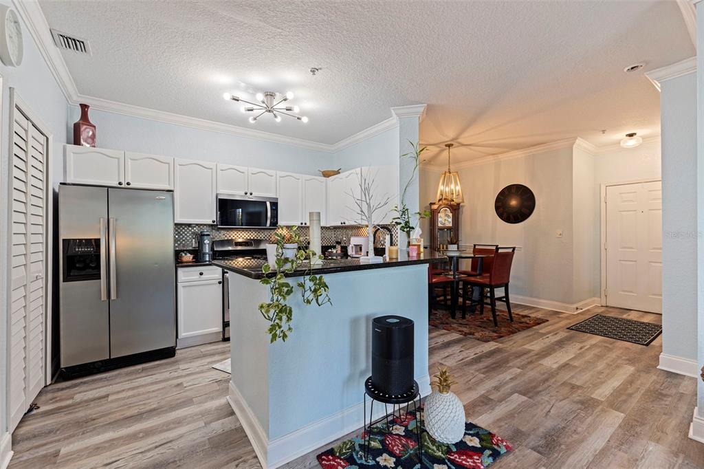 A kitchen with white cabinets, stainless steel appliances, and a breakfast bar opens to a dining area — 2773 VIA CIPRIANI UNIT 1321B, CLEARWATER, FL