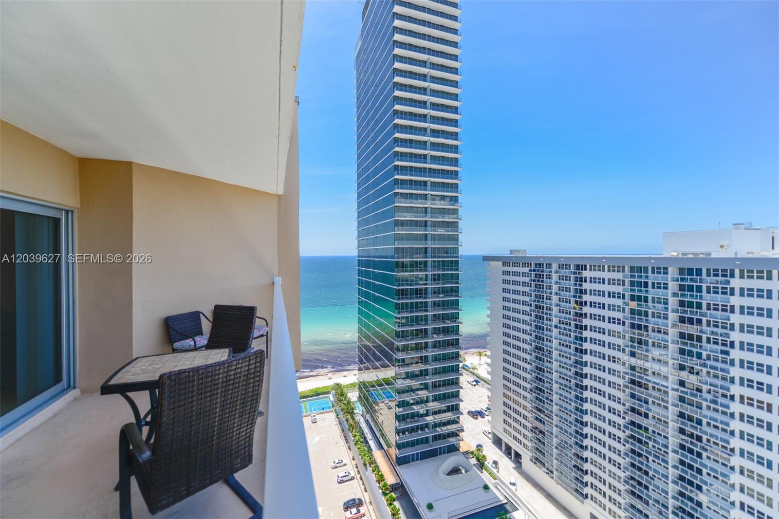 A balcony with outdoor furniture overlooks the ocean and nearby high-rise buildings — 1980 S Ocean Dr, Hallandale Beach FL 33009, HALLANDALE BEACH, FL