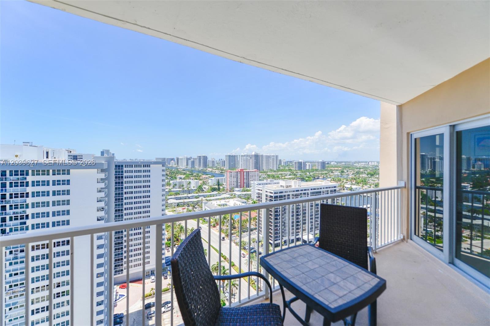 A balcony with a small table and two chairs overlooks a city skyline — 1980 S Ocean Dr, Hallandale Beach FL 33009, HALLANDALE BEACH, FL