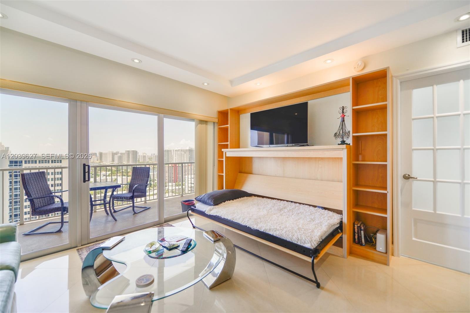 A living room features a Murphy bed, glass coffee table, and a balcony with city views — 1980 S Ocean Dr, Hallandale Beach FL 33009, HALLANDALE BEACH, FL
