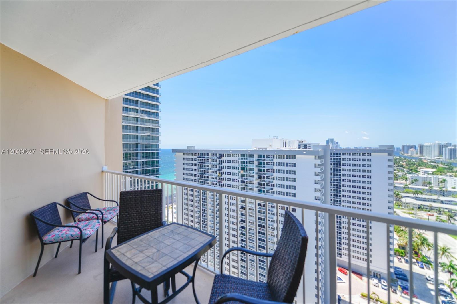 A balcony with patio furniture overlooks high-rise buildings and the ocean — 1980 S Ocean Dr, Hallandale Beach FL 33009, HALLANDALE BEACH, FL