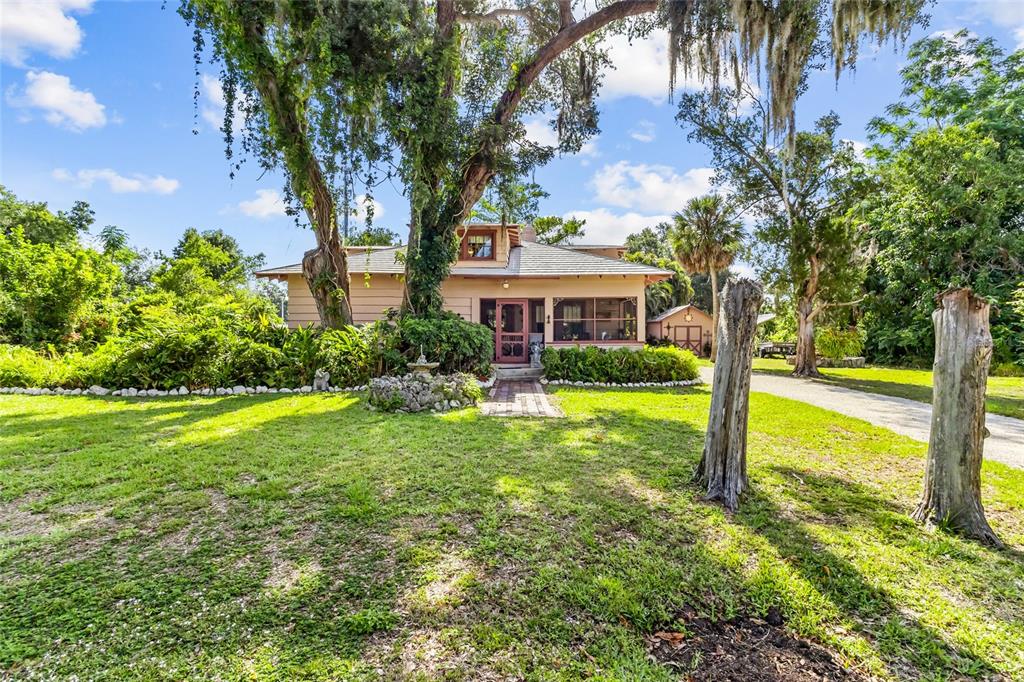 A single-story house with a screened porch sits behind a large tree and lawn — 117 TUCKER AVENUE, SARASOTA, FL