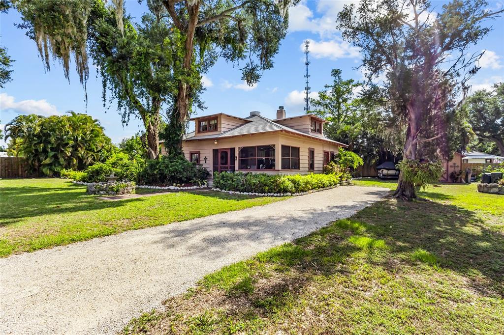 A single-story house with a gravel driveway, surrounded by large trees and lush landscaping — 117 TUCKER AVENUE, SARASOTA, FL