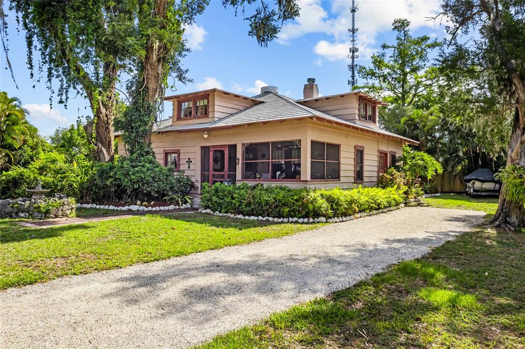A tan, single-story house with a gravel driveway and a screened-in front porch — 117 TUCKER AVENUE, SARASOTA, FL