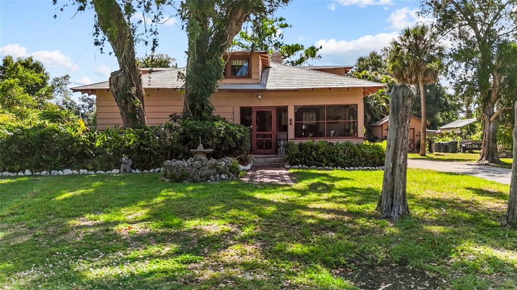 A single-story house with a screened porch, a stone fountain, and large trees in front — 117 TUCKER AVENUE, SARASOTA, FL