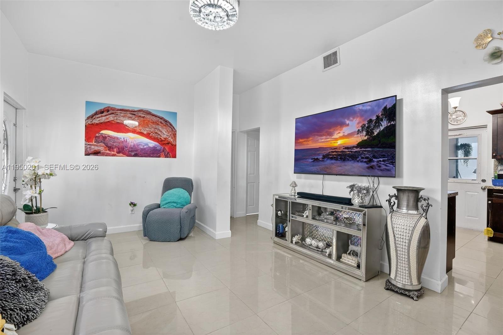A living room features a wall-mounted television, a mirrored media console, and tile flooring — 1240 Sharazad Blvd, Opa-Locka FL 33054, OPA-LOCKA, FL