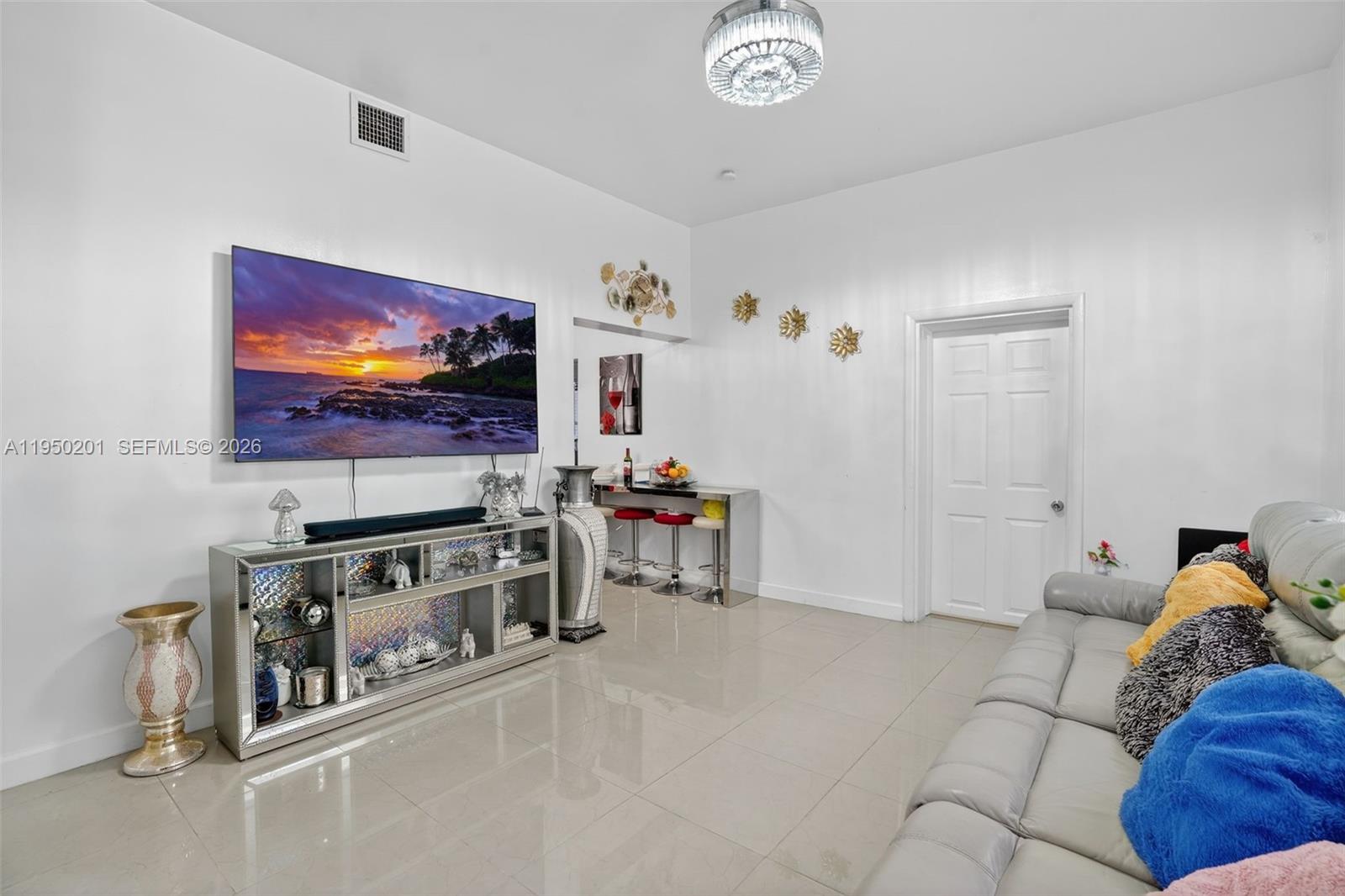 A living room features a large wall-mounted television, a mirrored media console, and tile flooring — 1240 Sharazad Blvd, Opa-Locka FL 33054, OPA-LOCKA, FL