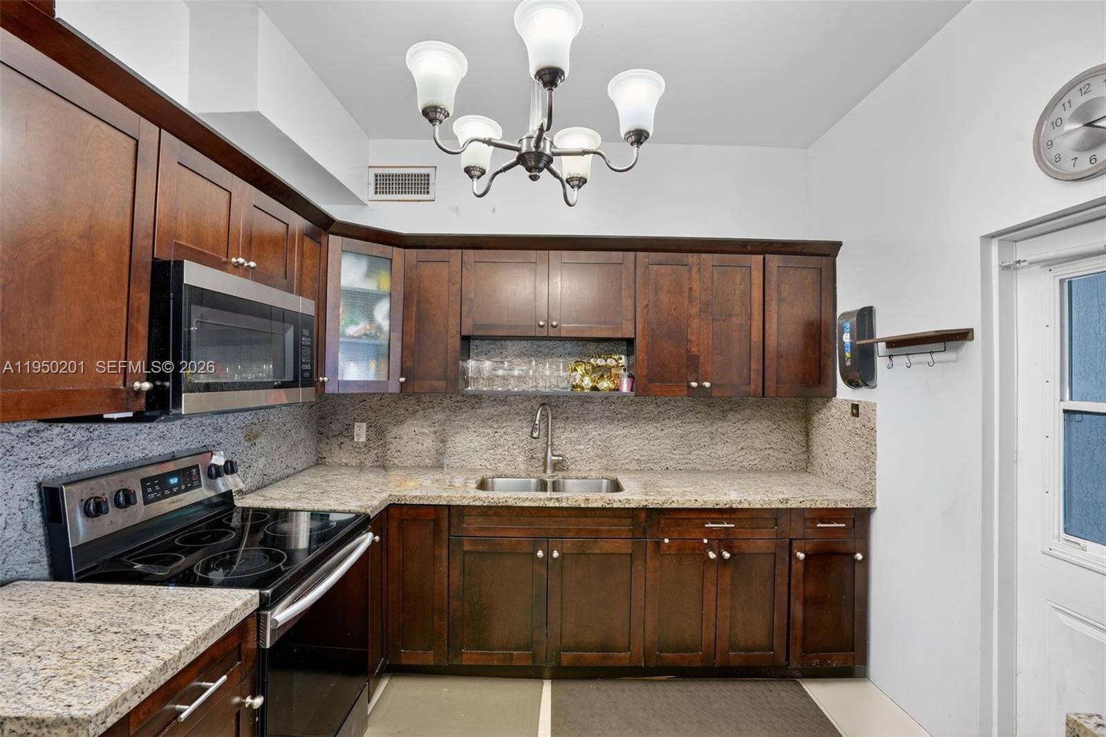 A kitchen features dark wood cabinets, granite countertops, a stainless steel stove, and a chandelier — 1240 Sharazad Blvd, Opa-Locka FL 33054, OPA-LOCKA, FL