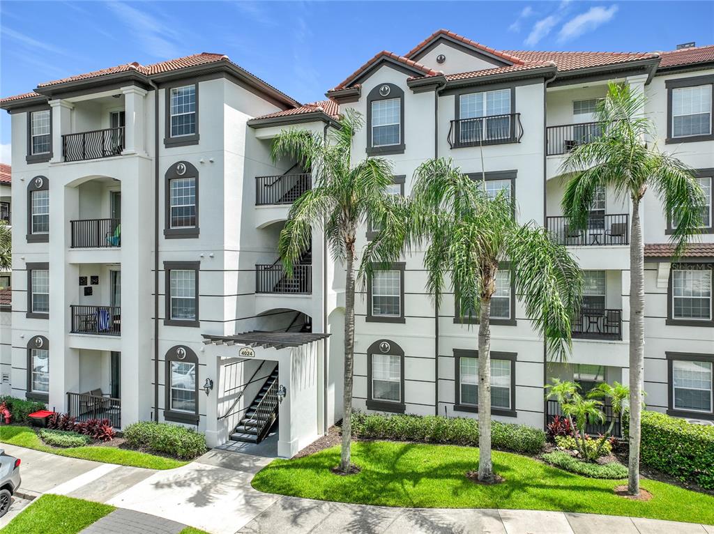 A multi-story apartment building exterior features white stucco walls, dark window frames, and palm trees — 4024 BREAKVIEW DRIVE UNIT 20904, ORLANDO, FL