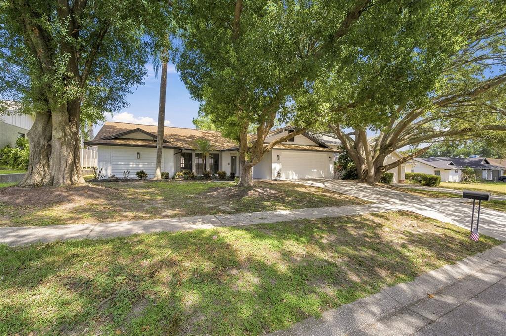 A single-story white house with a two-car garage sits behind large trees and a lawn — 2721 BRIARPATCH DRIVE, VALRICO, FL