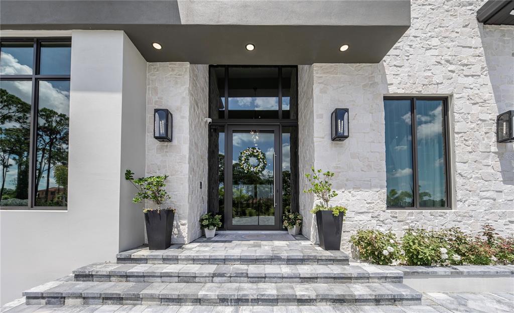 The front entrance features a glass door, stone facade, and tiered gray paver steps — 9240 FALCON COURT, VENICE, FL