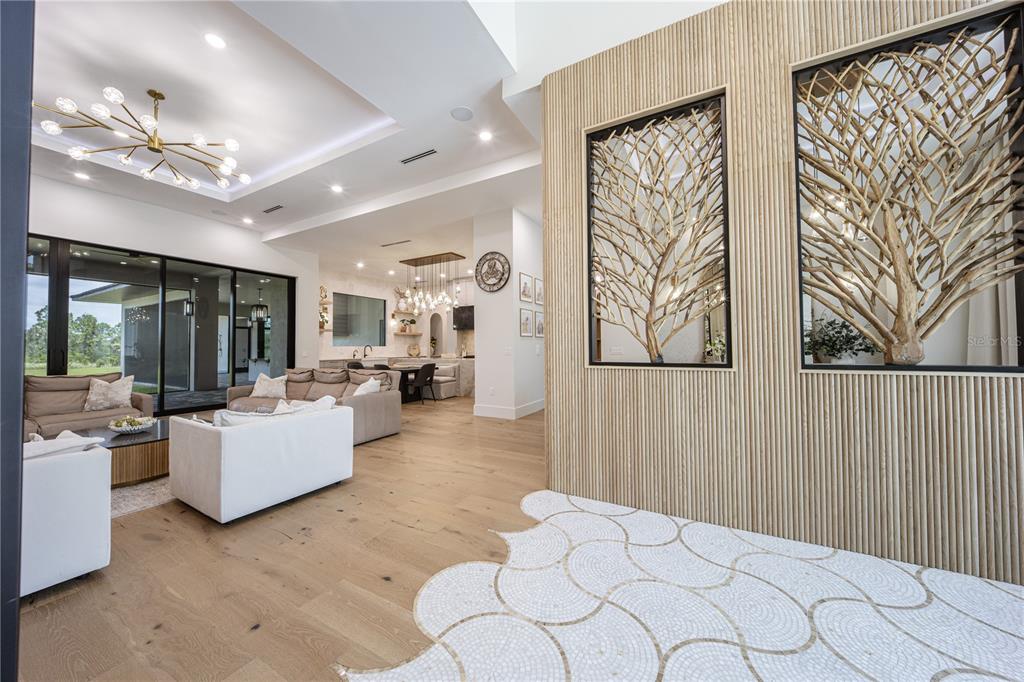 A modern living room features light wood floors, a decorative wall, and a large chandelier — 9240 FALCON COURT, VENICE, FL