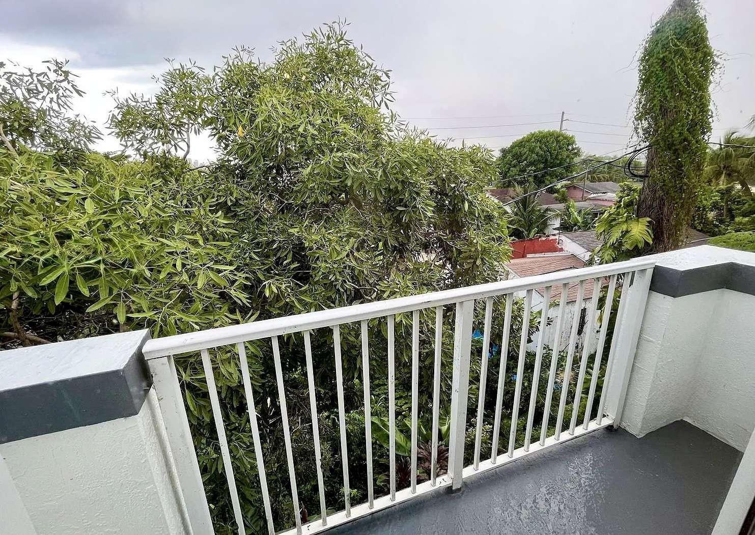 A balcony with a white metal railing overlooks a dense green tree and neighborhood rooftops — 7516 NE 1st Avenue # 302, Miami FL 33138, MIAMI, FL