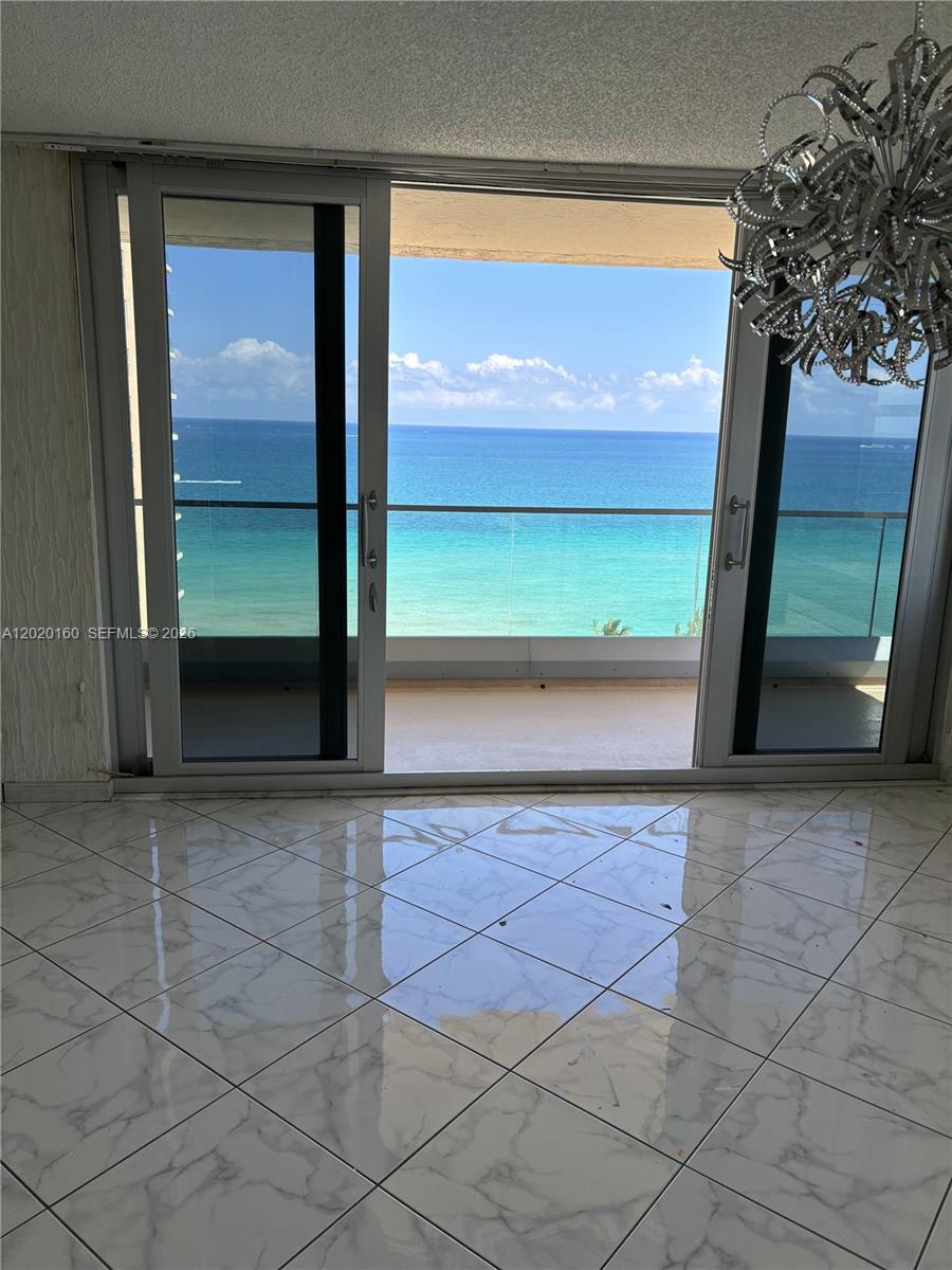 A room with white marble-patterned tile floors features sliding glass doors opening to an ocean view — 1920 S Ocean Dr # 16B, Hallandale Beach FL 33009, HALLANDALE BEACH, FL
