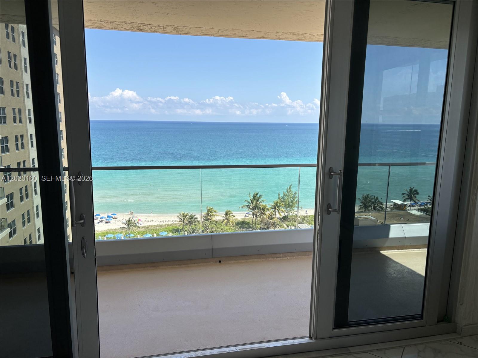 A view of the ocean and beach from a balcony through sliding glass doors — 1920 S Ocean Dr # 16B, Hallandale Beach FL 33009, HALLANDALE BEACH, FL