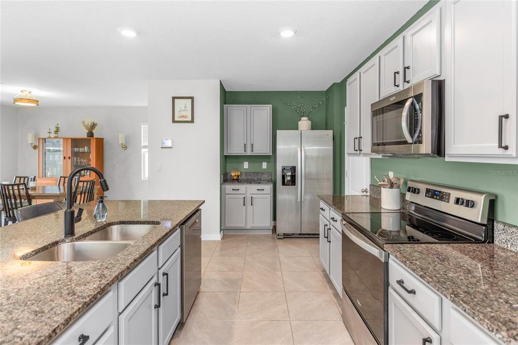 A kitchen features white and gray cabinets, granite countertops, stainless steel appliances, and green walls — 3758 SUNGROVE CIRCLE, SANFORD, FL