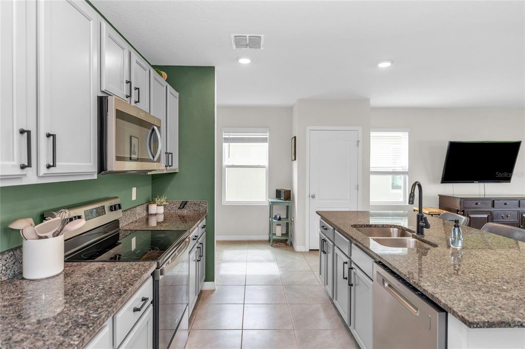 A kitchen features light gray cabinets, granite countertops, stainless steel appliances, and a green accent wall — 3758 SUNGROVE CIRCLE, SANFORD, FL