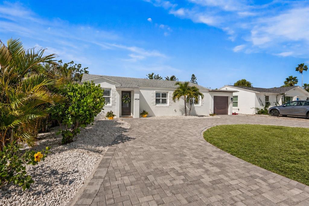 A single-story white house features a paved driveway, a front lawn, and tropical landscaping — 14024 N BAYSHORE DRIVE, MADEIRA BEACH, FL
