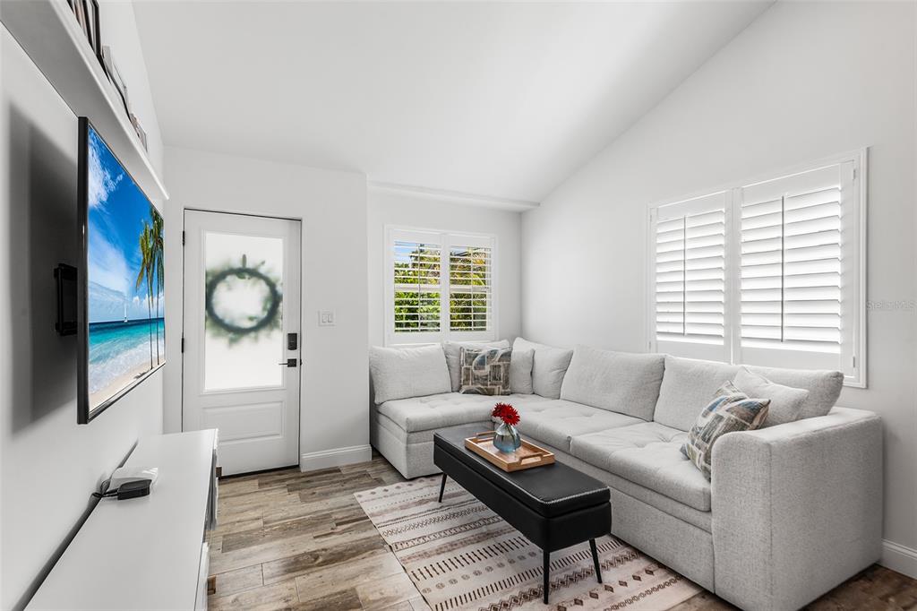 A living room features a sectional sofa, a television, and white plantation shutters on windows — 14024 N BAYSHORE DRIVE, MADEIRA BEACH, FL