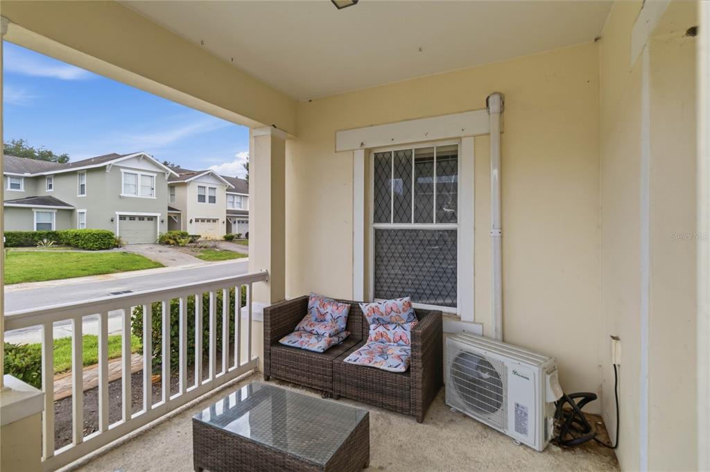 A covered porch features a wicker loveseat, a glass-topped table, and an outdoor air conditioner — 2041 LACIE JO LANE, KISSIMMEE, FL